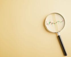 A magnifying glass lying on a beige surface, focusing on a candlestick stock chart with red and green bars visible inside the lens.