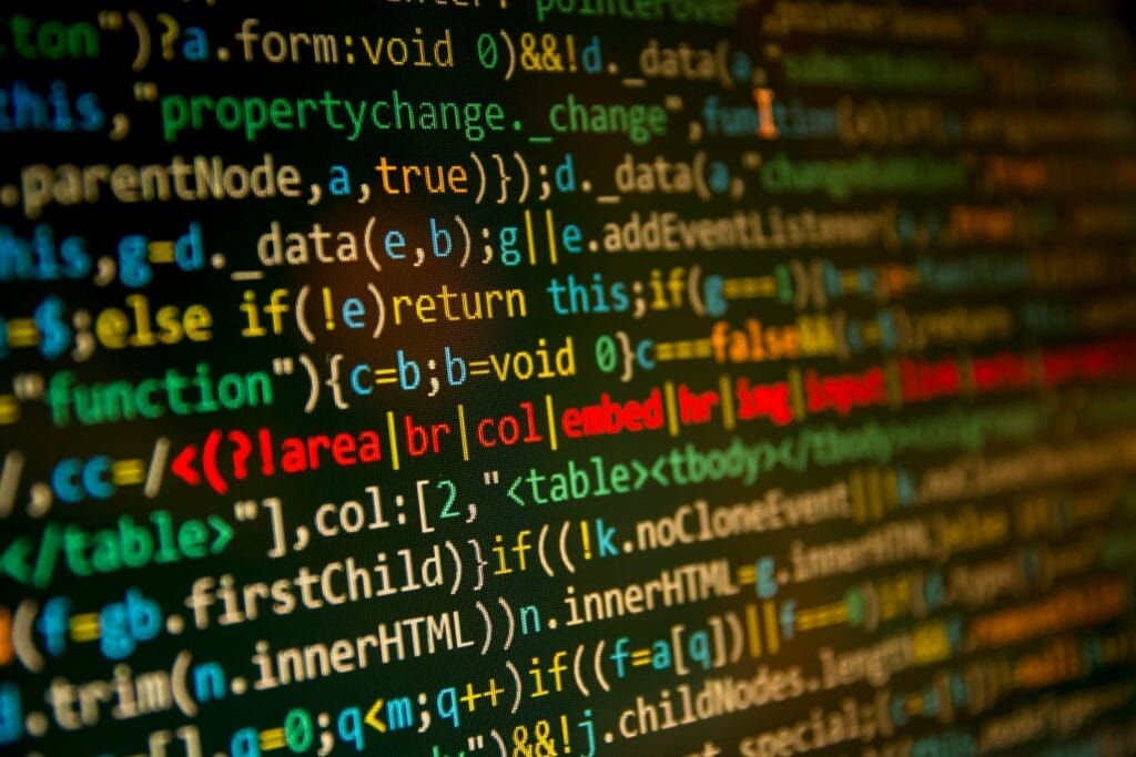 Close-up of a computer screen displaying colorful lines of code with various programming symbols, functions, and highlighted text on a dark background.