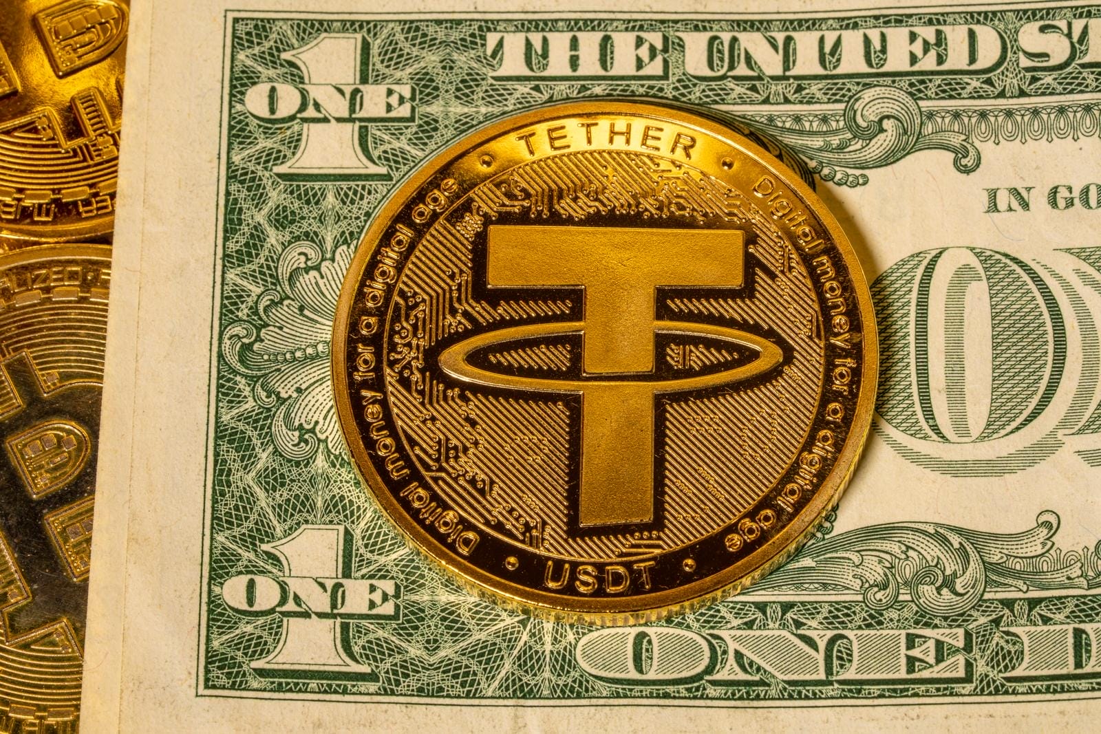 A gold Tether (USDT) cryptocurrency coin is placed on top of a U.S. one-dollar bill, partially covering the bill's details.